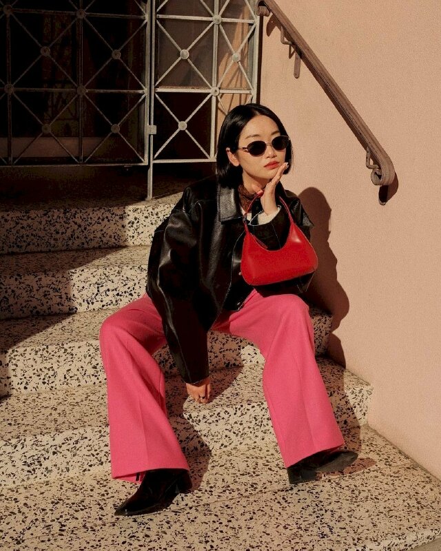 Tạo dáng ngồi thoải mái, tay cầm túi chống cằm