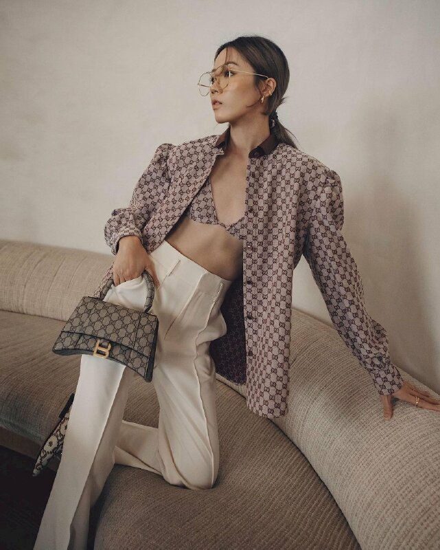 Tạo dáng đứng nghiêng người một chân gác lên ghế hay sofa, một chân duỗi thẳng, một tay vin thành ghế, một tay cầm chiếc túi thời trang và đút túi quần, mặt quay nghiêng