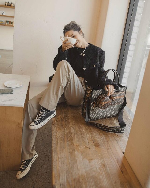 Tạo dáng ngồi một chân co gác lên, một chân co duỗi, một tay để nhẹ lên chiếc túi thời trang kế bên, một tay cầm một cái gì đó đưa lên che một phần gương mặt