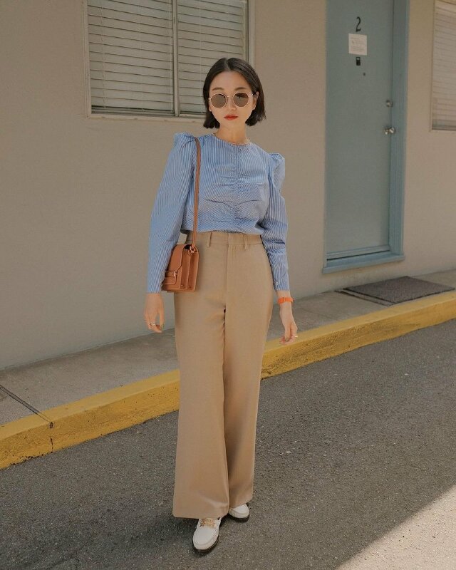 Tạo dáng đứng thẳng tự nhiên với một chân hơi hướng nhẹ phía trướng, hai tay buông thẳng, túi xách đeo một bên vai với độ dài ngang hông