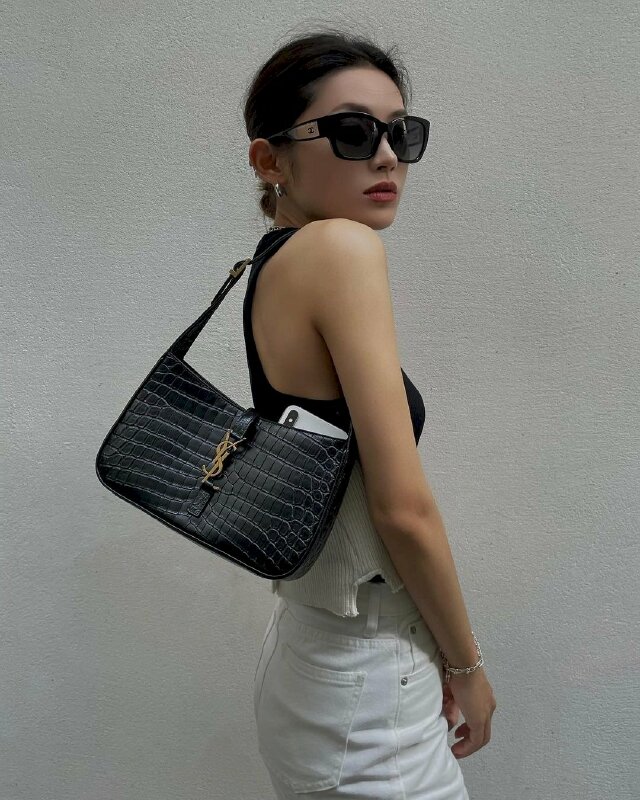 Tạo dáng mặt hướng về ống kính biểu cảm lạnh lùng, hai tay để phía trước thật tự nhiên, túi xách đeo vai đẩy túi ra sau