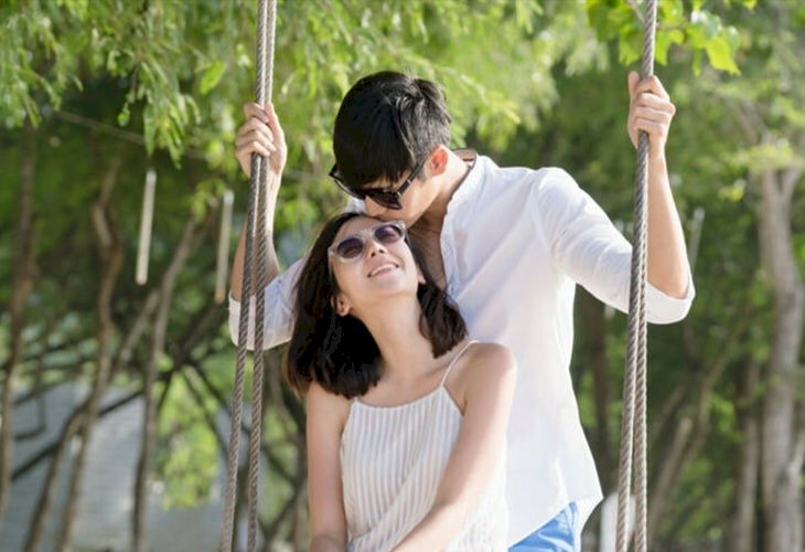 Tạo dáng cô gái ngồi trên xích đu, khẽ ngước mặt lên, chàng trai đứng phía sau nhẹ đặt nụ hôn lên trán cô gái