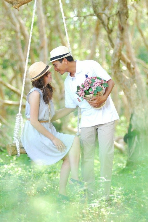 Tạo dáng cô gái mặc một chiếc váy nhẹ nhàng ngồi trên xích đu khẽ hướng mặt lên, chàng trai với trang phục lịch lãm một tay ôm hoa, một tay vịn nhẹ eo cô gái, thân người hơi cúi như chuẩn bị hôn cô gái