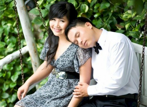 Tạo dáng ngồi tự nhiên trên xích đu, cô gái hướng mắt nhìn lên máy ảnh cười thật tươi, chàng trai tựa đầu vào vai cô gái với đôi mắt nhắm