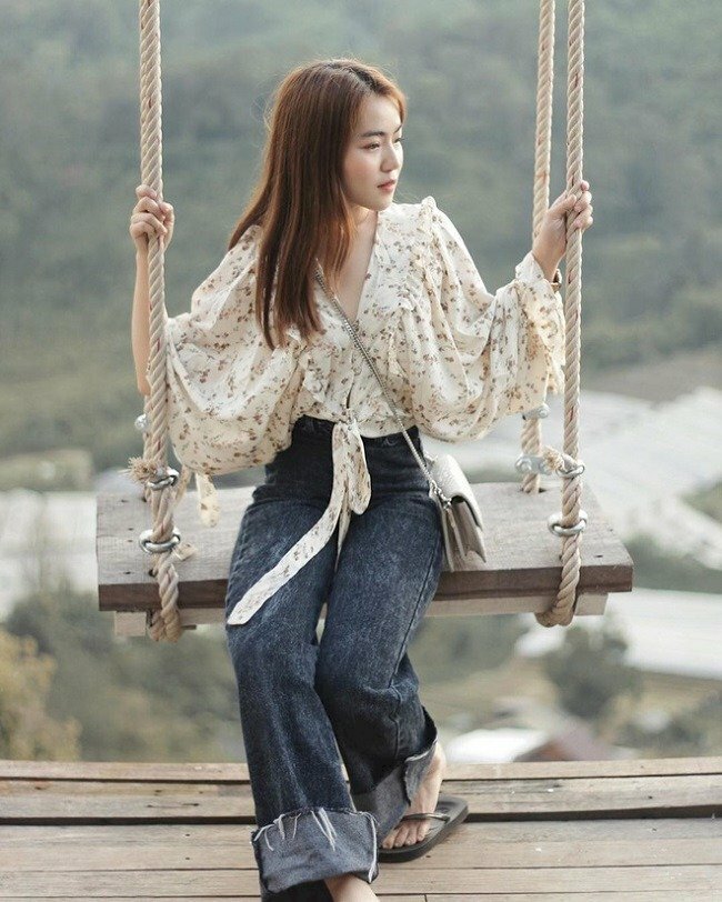 Tạo dáng ngồi tự nhiên trên xích đu, hai chân chéo nhẹ, hai tay vịn dây xích đu, mặt quay nghiêng