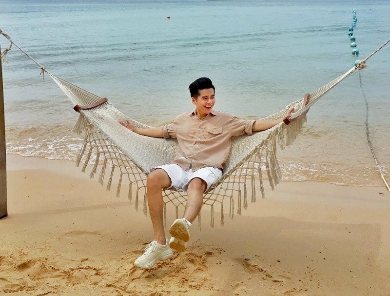 Tạo dáng ngồi một cách thoải mái với thân người ngả về sau, hai tay dang rộng sang ngang, chân thả tự nhiên, mặt khẽ quay nghiêng cười thật tươi