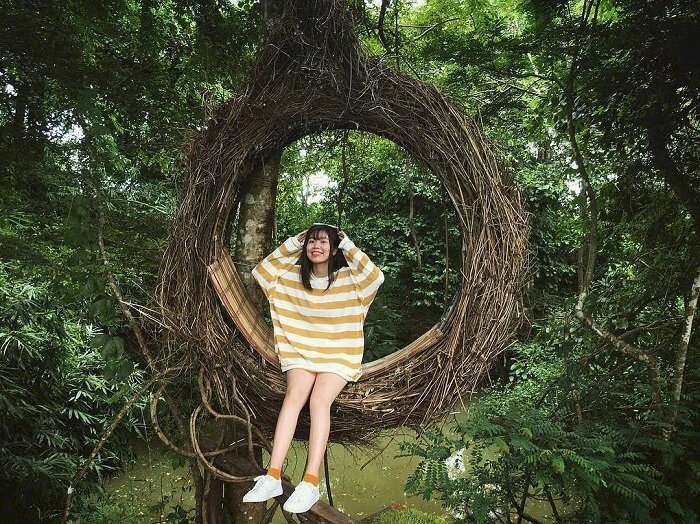 Tạo dáng ngồi trên xích đu với hai chân duỗi tự nhiên, hai tay nhẹ đưa lên chạm tóc, mặt nhìn ống kính hơi hướng cằm lên nở nụ cười dễ thương