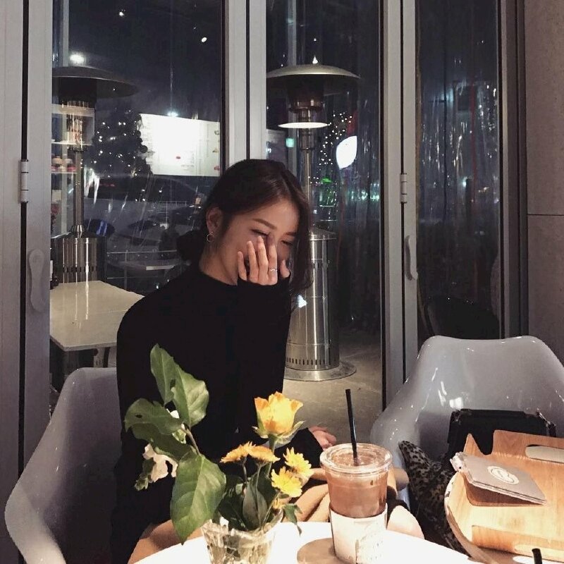 Tạo dáng ngồi tự nhiên trên ghế, một tay để trên đùi, một tay đưa lên che mặt đang cười