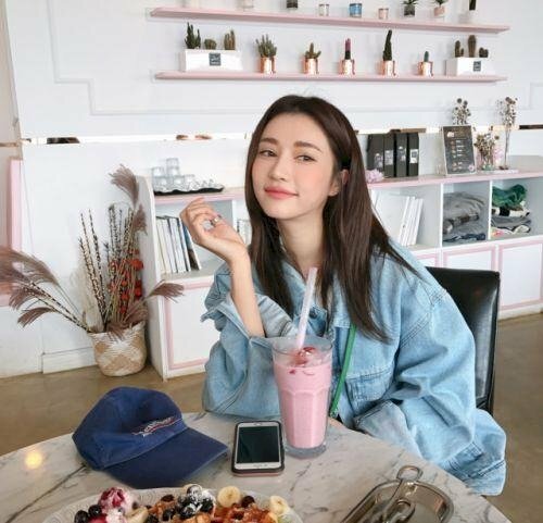 Tạo dáng ngồi tự nhiên, một tay để trên đùi, một tay chống trỏ trên bàn, đầu hơi nghiêng hướng cằm lên, cười dễ thương