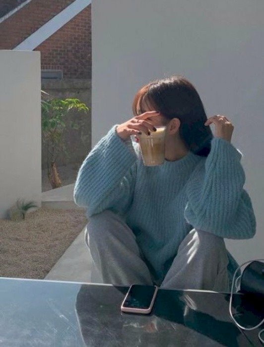 Tạo dáng đầu quay nghiêng nhìn sang một phía, hai chân co lên trên ghế, hai tay đặt trỏ lên đầu gối, một tay cầm ly trà sữa che mặt