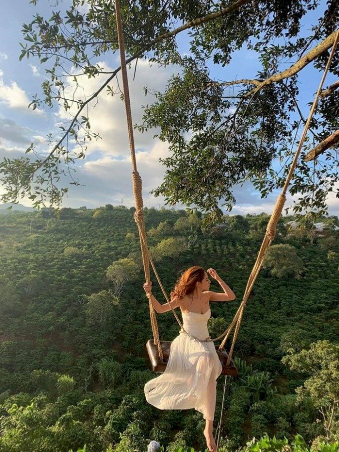 Tạo dáng ngồi xích đu hai chân chéo, một tay vịn dây xích đu, một tay nhẹ đưa lên vuốt tóc, tóc dài để xoã bay trong gió, mặt quay nghiêng