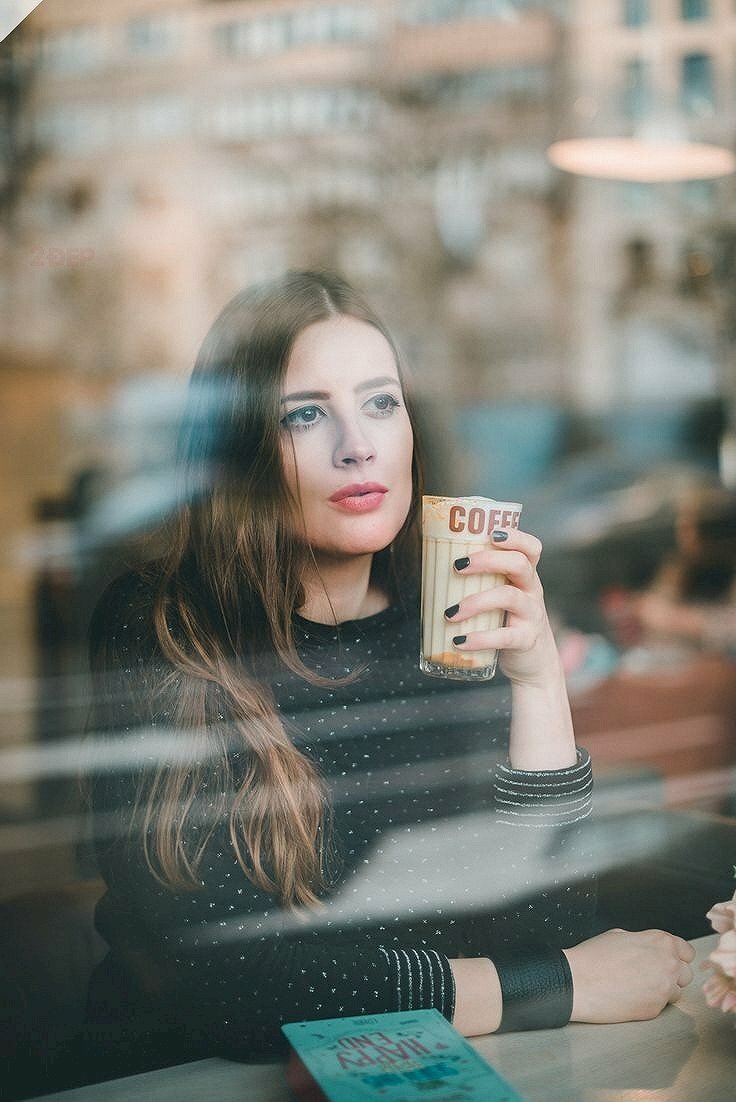 Kiểu tạo dáng ngồi với một tay cầm ly trà sữa, một tay khoanh đặt trên bàn, mặt hướng lên với ánh mắt nhìn xa xăm tư lự