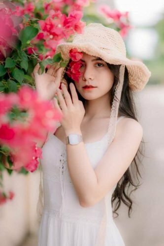 Tạo dáng dùng cành hoa giấy che mặt, mắt nhìn thẳng về phía ống kính