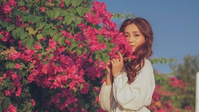 Tạo dáng nép mình vào giàn hoa giấy, dùng 02 tay nhẹ nhàng nâng cành hoa che mặt