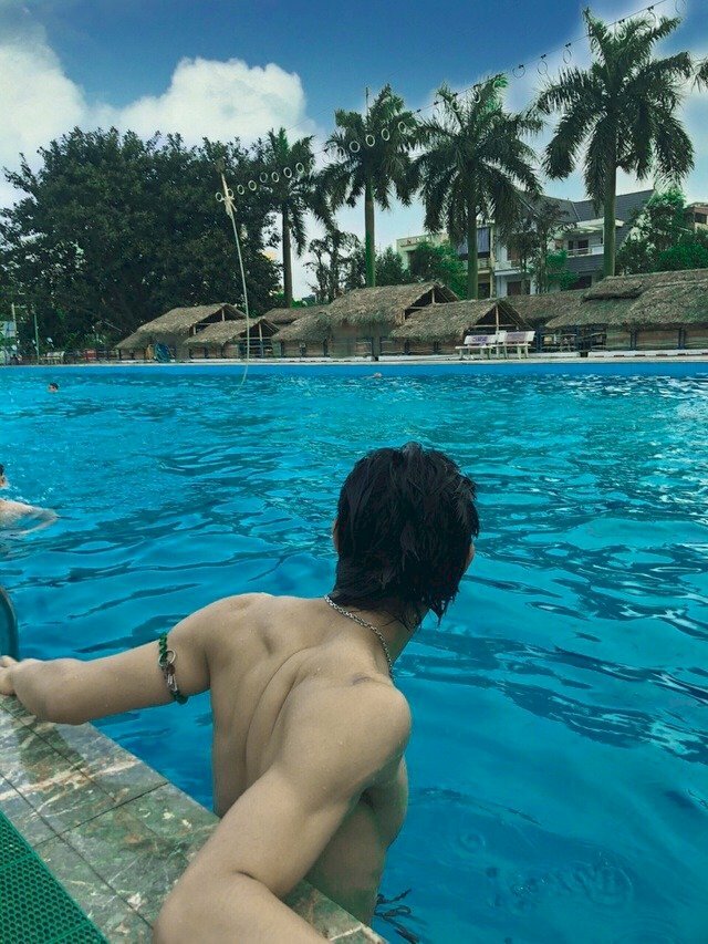 Tạo dáng đứng tựa thành bể bơi, hai tay dang rộng sang ngang gác lên thành bể bơi, mặt hơi quay nghiêng