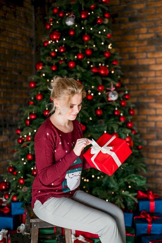 Cách tạo dáng chụp ảnh với cây thông Noel của người phụ nữ tay cầm hộp quà, đầu cúi nhìn, miệng mìm cười