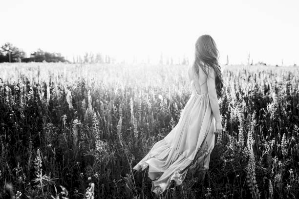 Ảnh đẹp trắng đen cô gái trong chiếc đầm dài thướt tha quay lưng bước đi trên cánh đồng hoa như muốn thả bay mọi nỗi muộn phiền trong gió chiều