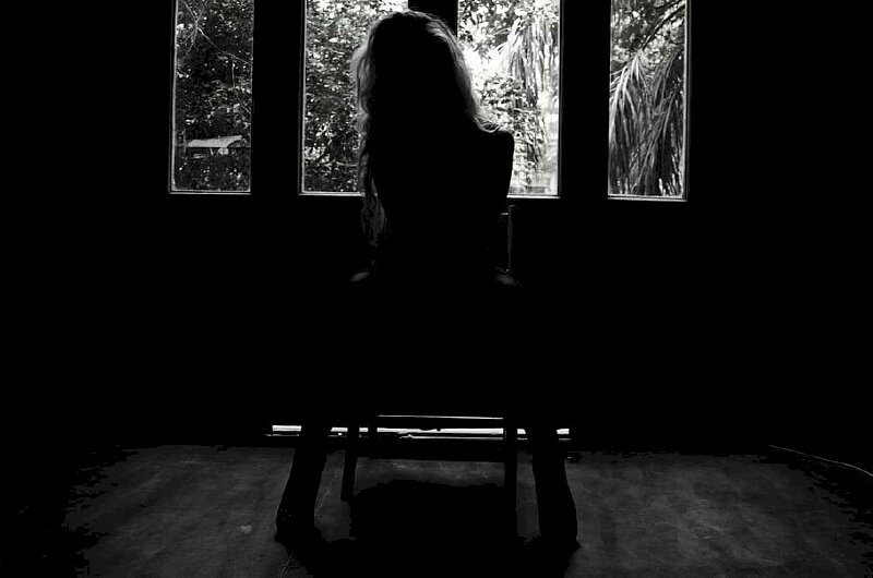 Ảnh trắng đen cô gái ngồi quay lưng trên ghế trong căn phòng tối với nhiều tâm sự buồn