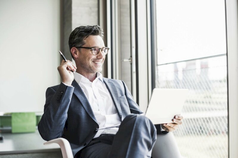 Hình ảnh người đàn ông thành đạt ngồi làm việc thật thoải mái, nụ cười tự tin