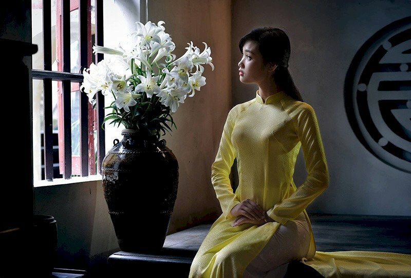 Hình ảnh đẹp nhẹ nhàng thiếu nữ trong tà áo dài thướt tha ngồi bên bình hoa loa kèn trắng